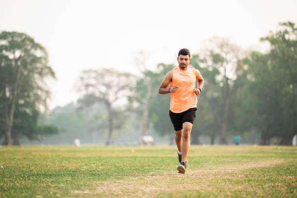 Young athletic man running at park during summer morning. Sport fitness model training outdoor for marathon. City fitness. Running in the park.